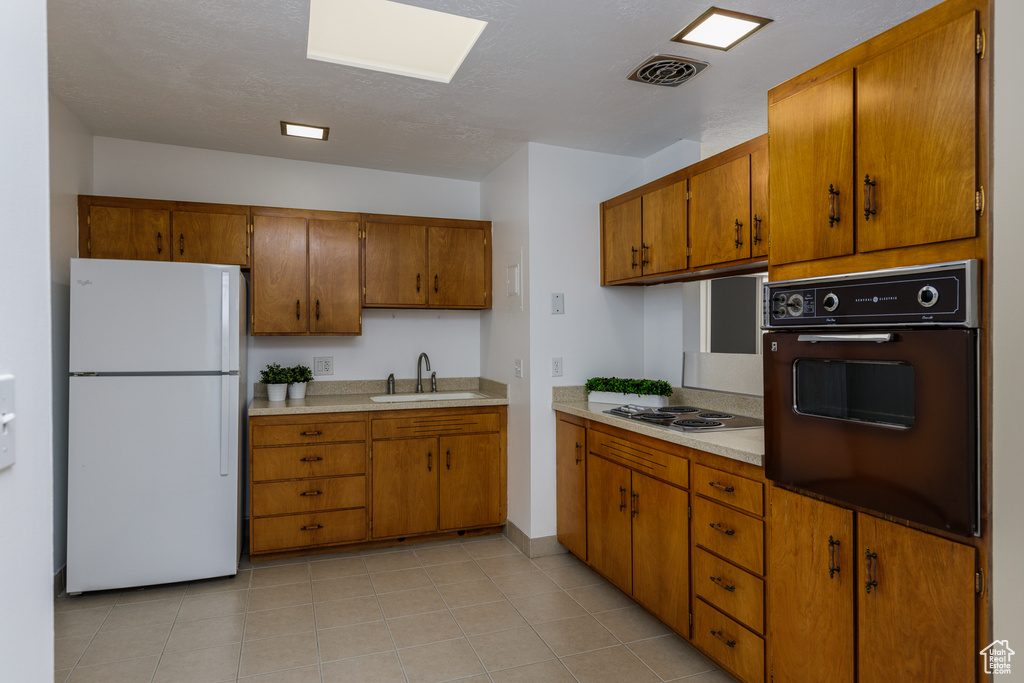 Kitchen with electric stovetop, sink, light tile floors, white refrigerator, and black oven