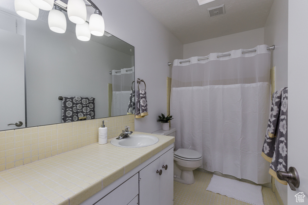 Bathroom with tasteful backsplash, vanity with extensive cabinet space, tile floors, and toilet