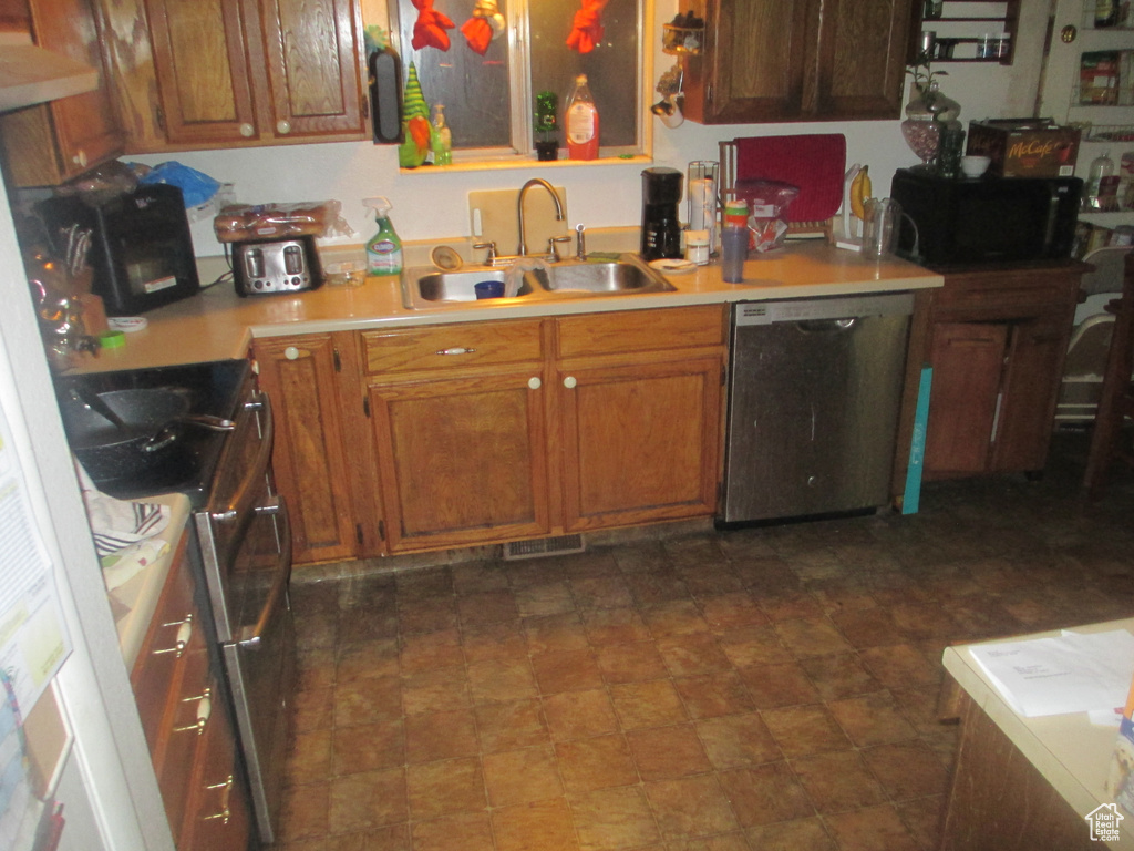 Kitchen with range, dark tile flooring, sink, wall chimney range hood, and dishwasher