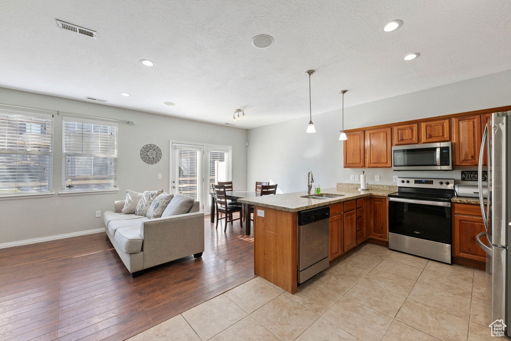 Kitchen featuring light tile floors, stainless steel appliances, kitchen peninsula, and decorative light fixtures