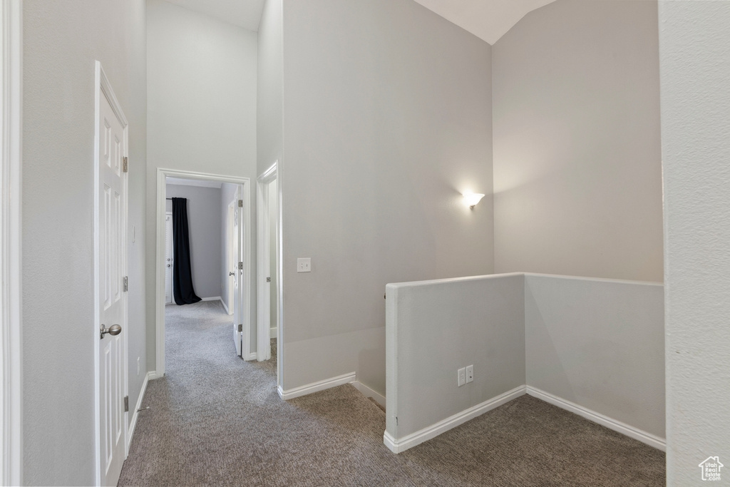 Hallway with vaulted ceiling and light colored carpet