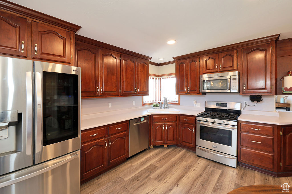 Kitchen with appliances with stainless steel finishes, light wood-type flooring, ornamental molding, and sink