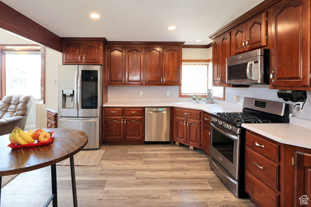 Kitchen featuring ornamental molding, appliances with stainless steel finishes, light wood-type flooring, and sink