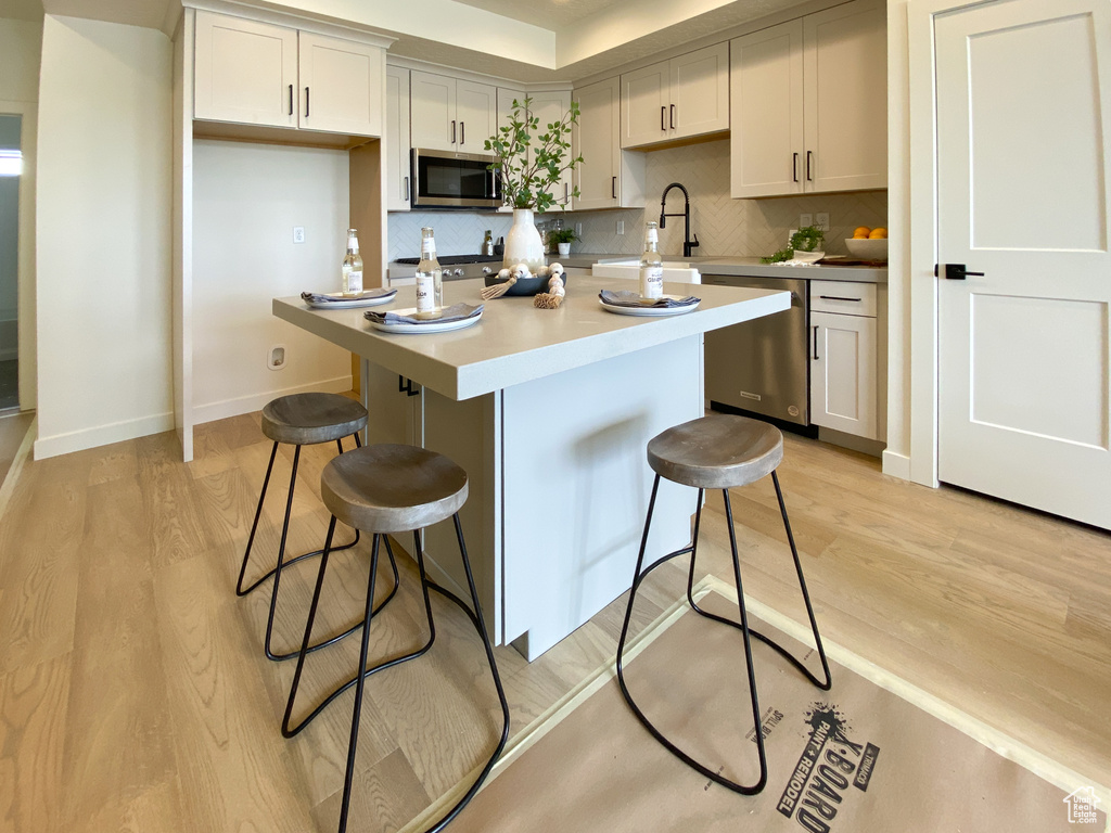 Kitchen with appliances with stainless steel finishes, light hardwood / wood-style flooring, a breakfast bar, and a kitchen island