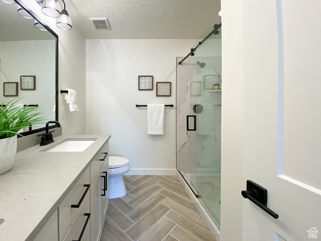 Bathroom featuring a textured ceiling, toilet, vanity, and walk in shower