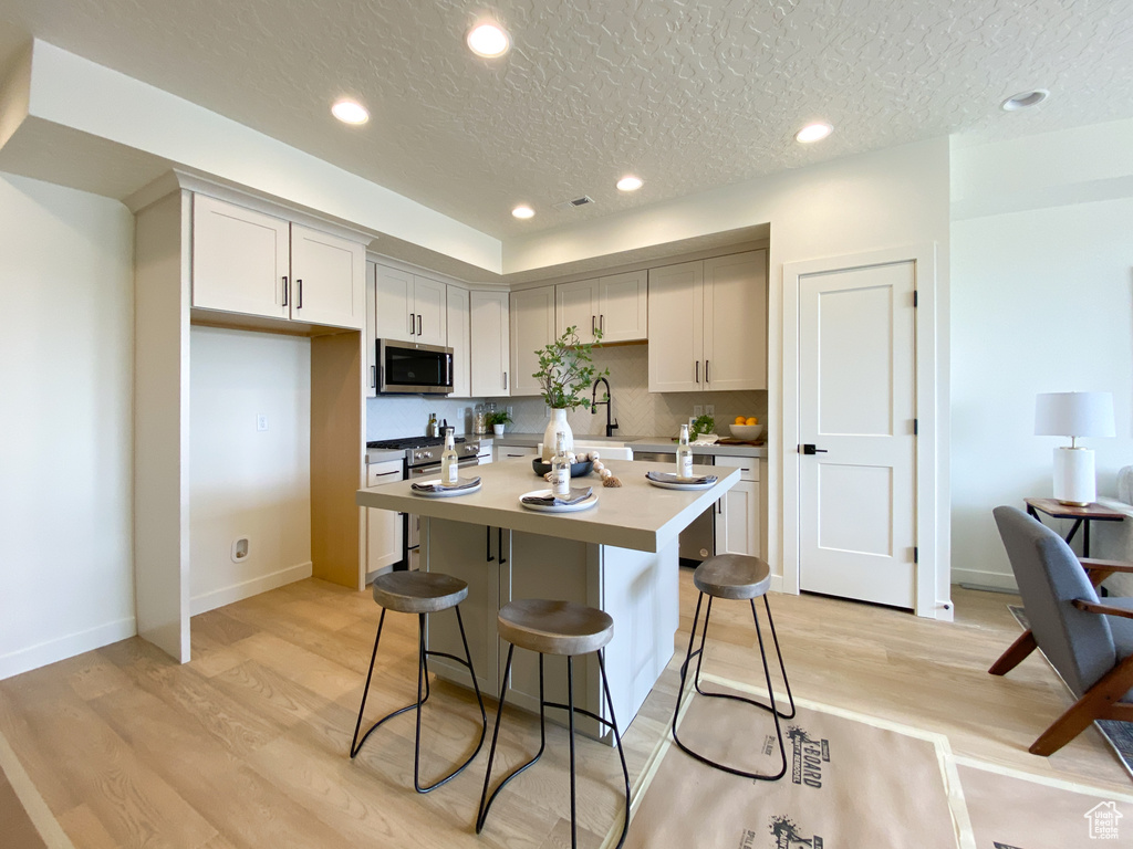 Kitchen with appliances with stainless steel finishes, light hardwood / wood-style floors, a kitchen breakfast bar, and a center island with sink