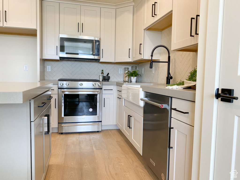 Kitchen with sink, light hardwood / wood-style flooring, backsplash, and stainless steel appliances