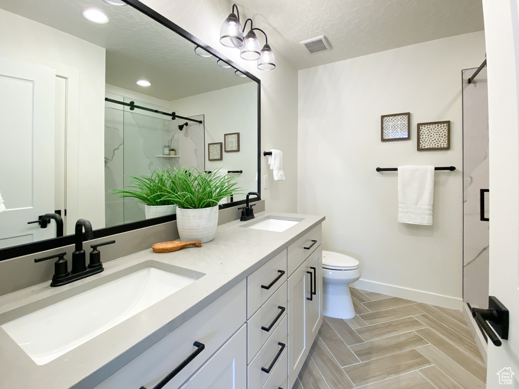 Bathroom with a textured ceiling, dual bowl vanity, tile floors, an enclosed shower, and toilet