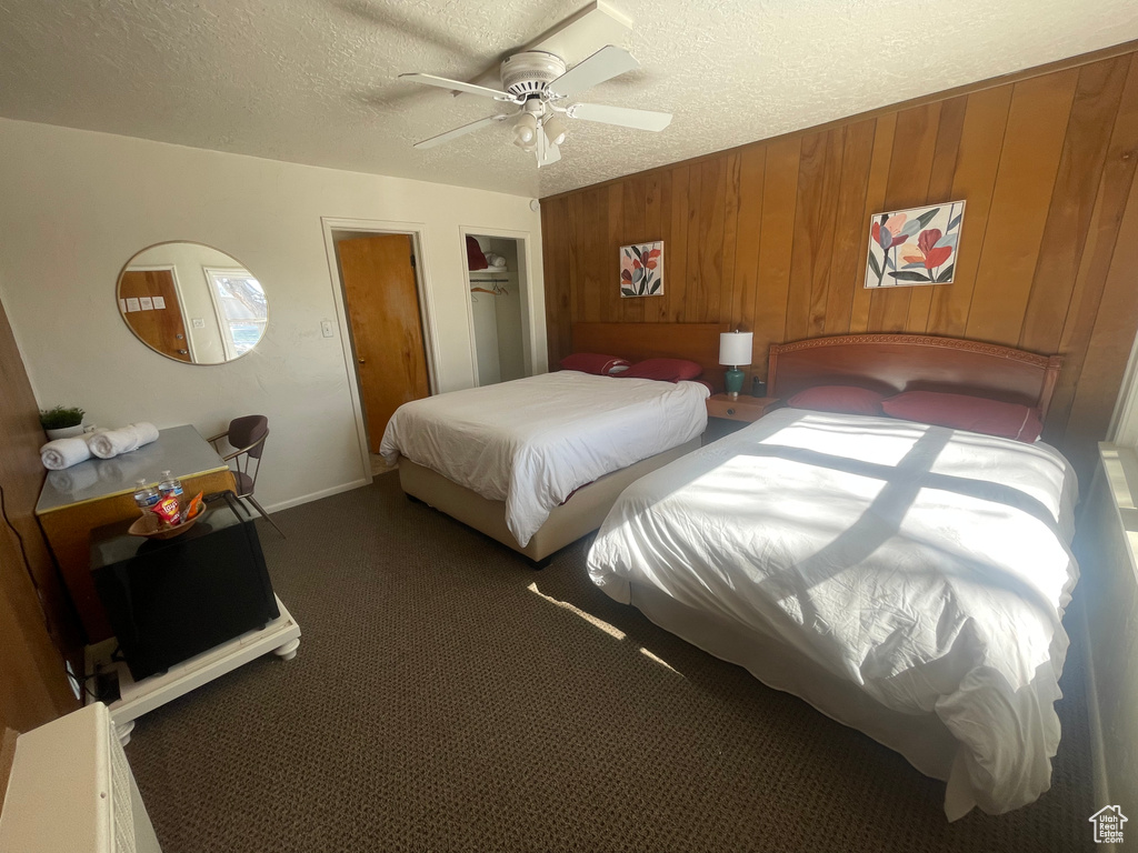 Carpeted bedroom with wood walls, a textured ceiling, and ceiling fan