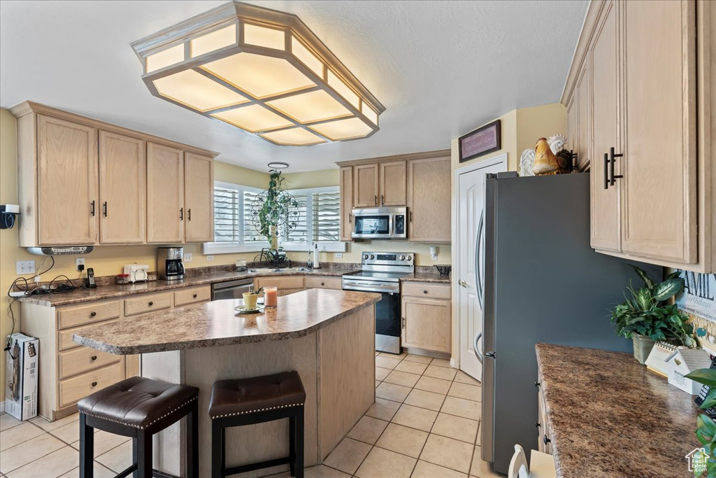 Kitchen with light tile flooring, sink, a kitchen bar, appliances with stainless steel finishes, and a center island