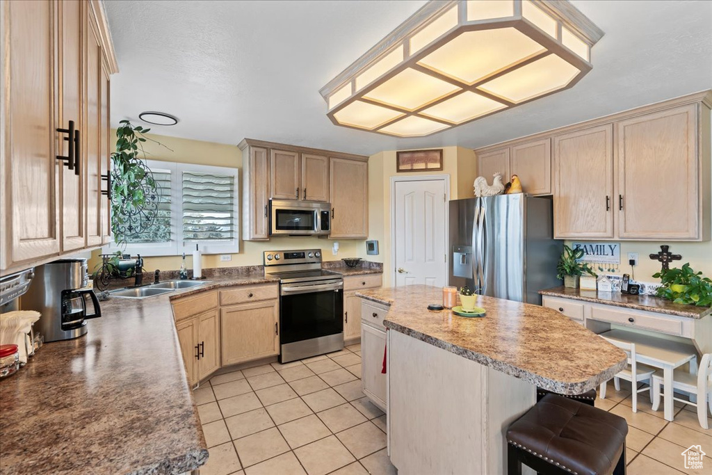 Kitchen featuring light brown cabinetry, light tile floors, stainless steel appliances, and a center island