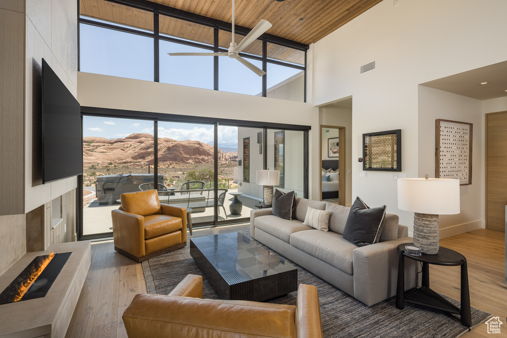 Living area with high vaulted ceiling, a ceiling fan, wood finished floors, a fireplace with raised hearth, and wooden ceiling