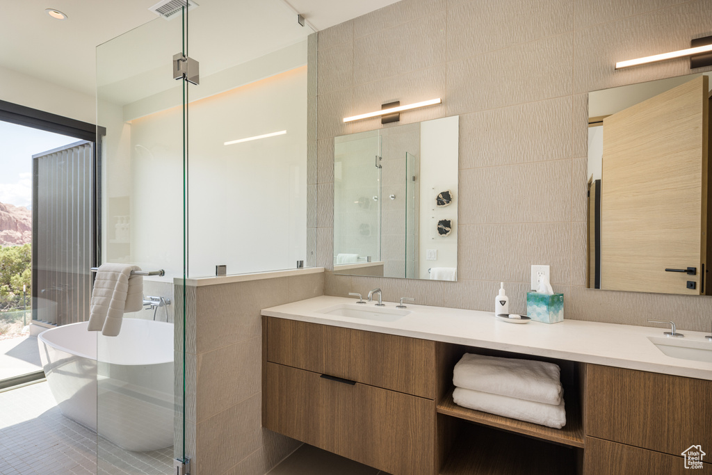 Full bath featuring double vanity, a shower stall, a freestanding tub, and tile walls