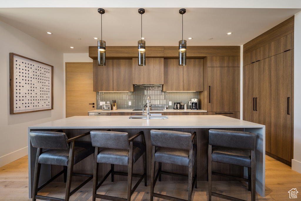 Kitchen featuring modern cabinets, brown cabinetry, backsplash, a kitchen island with sink, and recessed lighting