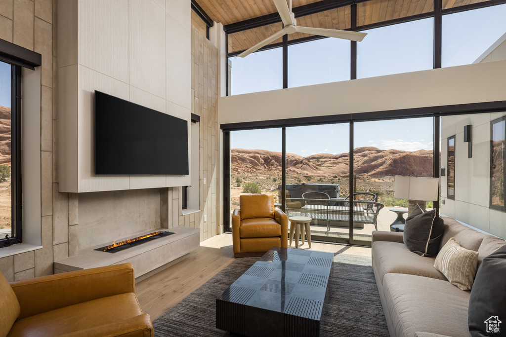 Living area featuring a fireplace with raised hearth, wood finished floors, high vaulted ceiling, healthy amount of natural light, and beamed ceiling