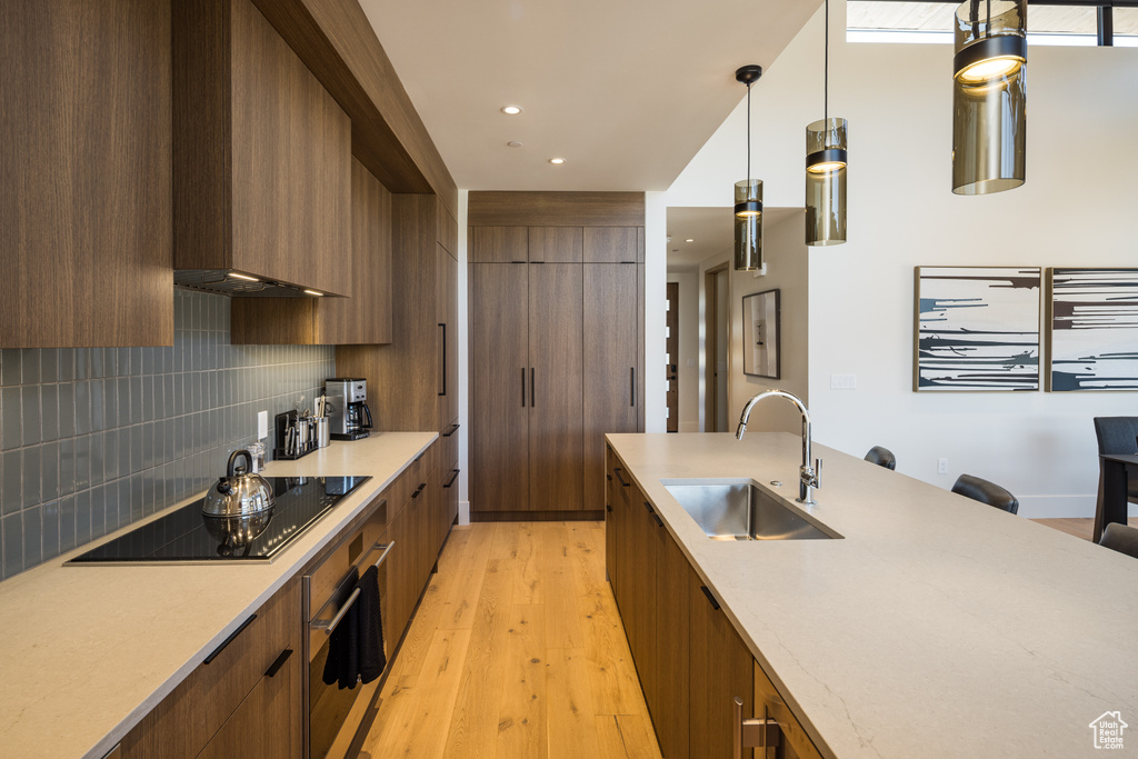 Kitchen featuring modern cabinets, black electric stovetop, light wood-style flooring, decorative backsplash, and hanging light fixtures