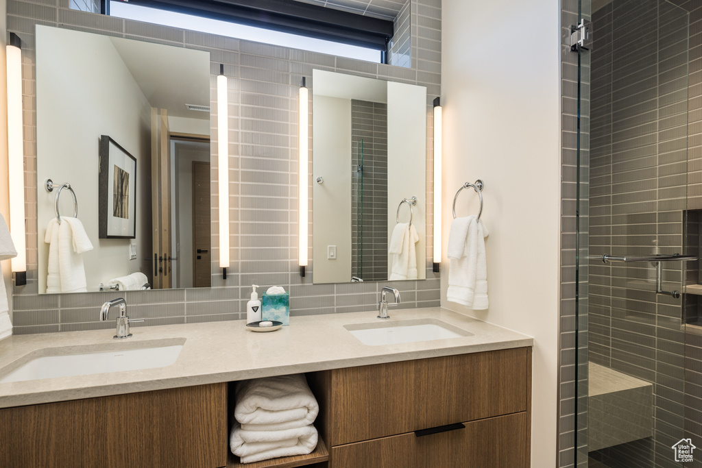 Bathroom with double vanity, tasteful backsplash, and tiled shower