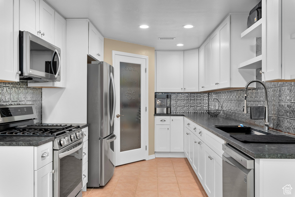 Kitchen with tasteful backsplash, light tile floors, stainless steel appliances, white cabinetry, and sink
