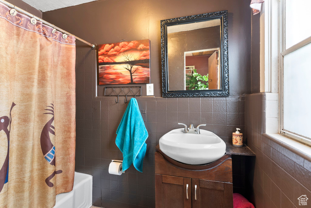 Bathroom with vanity, shower / tub combo, tasteful backsplash, and tile walls