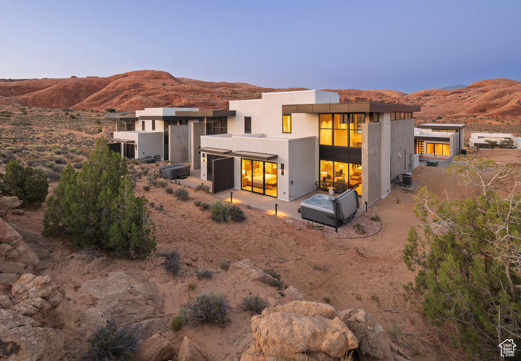 Back of property at dusk with a mountain view, a patio area, and a hot tub