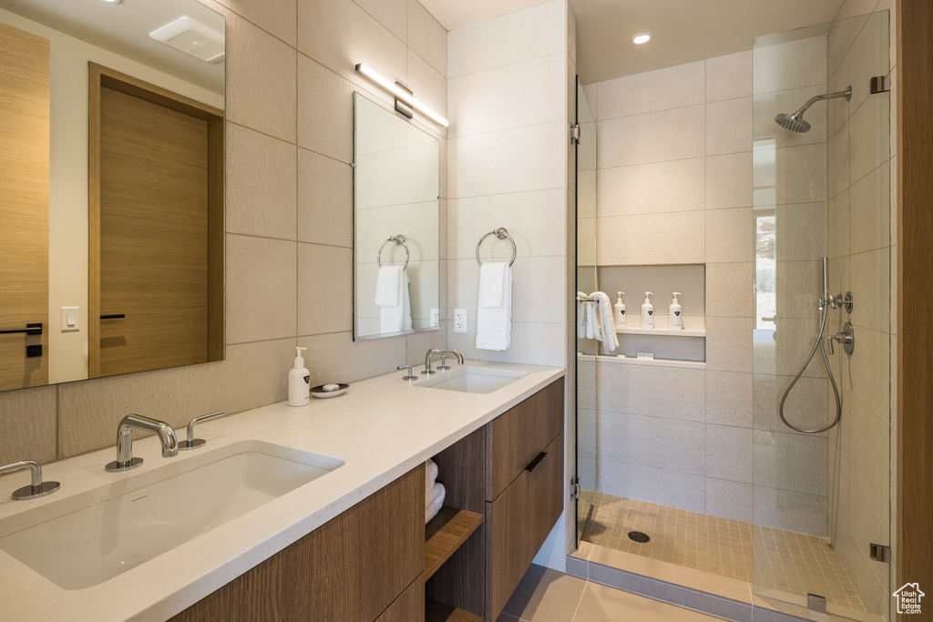 Bathroom with tiled shower, double vanity, recessed lighting, and tile walls
