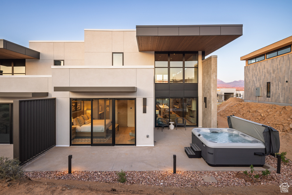 Back of property at dusk with a hot tub, a patio area, and a mountain view