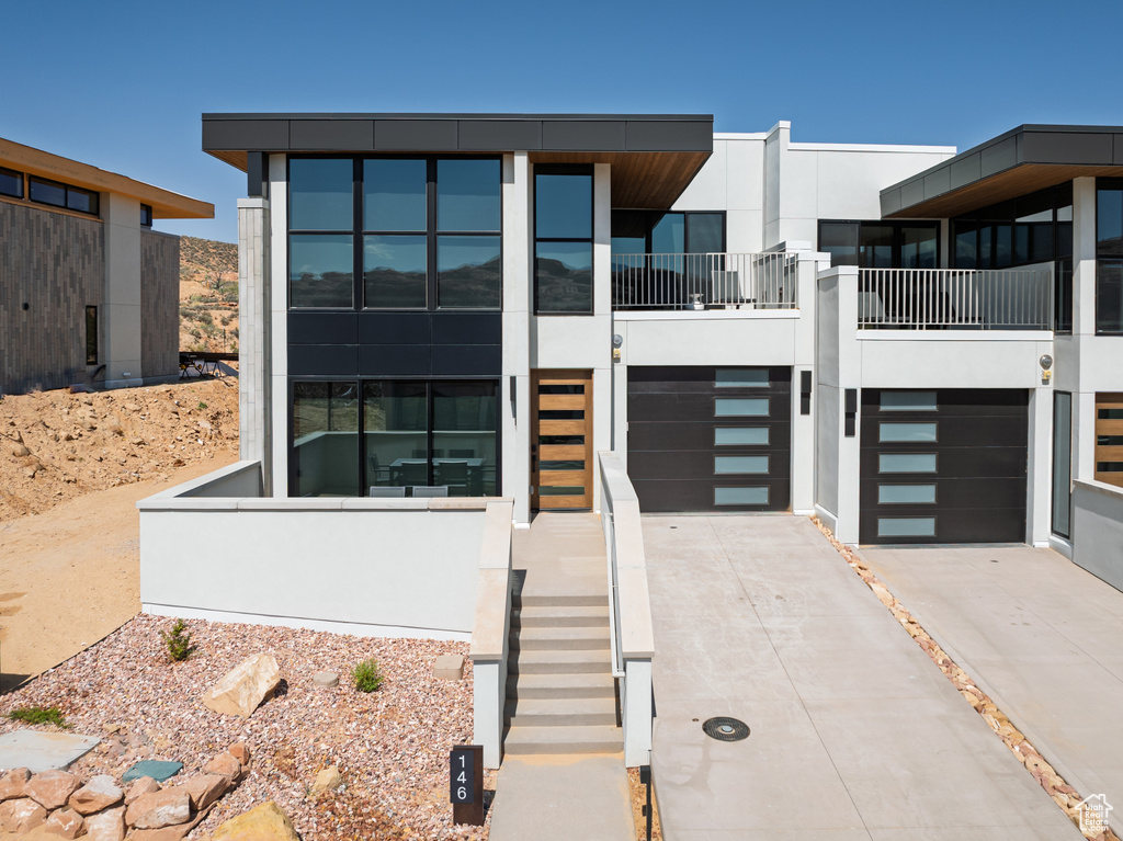 View of front facade with driveway, an attached garage, stucco siding, and stairs