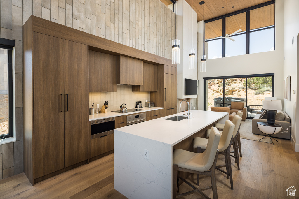 Kitchen featuring a towering ceiling, modern cabinets, light countertops, a center island with sink, and wood finished floors