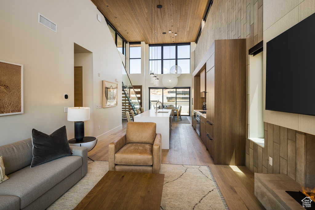 Living area with a towering ceiling, stairway, light wood-style flooring, and wood ceiling