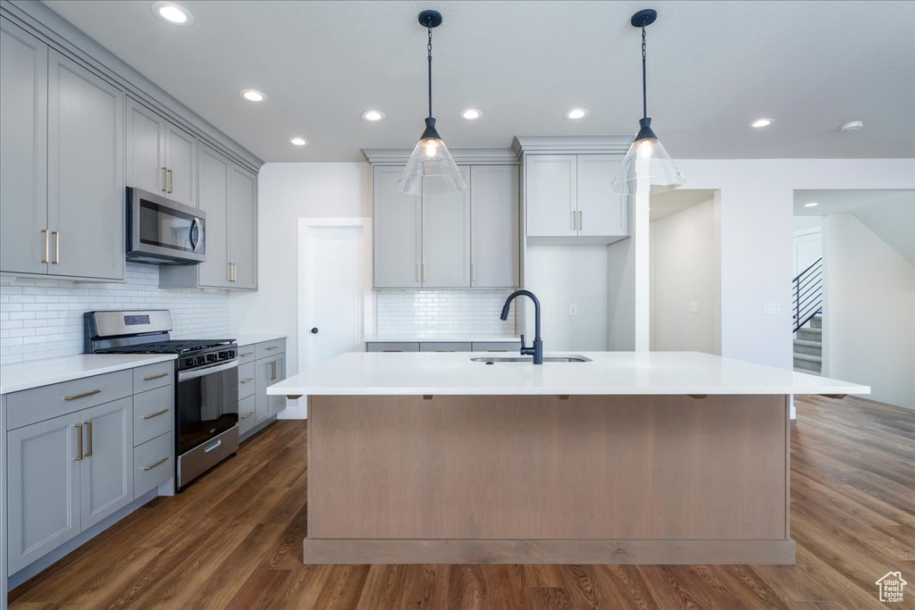 Kitchen featuring dark wood-type flooring, appliances with stainless steel finishes, an island with sink, and tasteful backsplash
