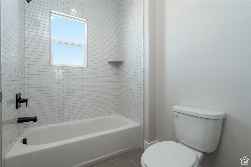 Bathroom featuring toilet, tiled shower / bath combo, and tile flooring