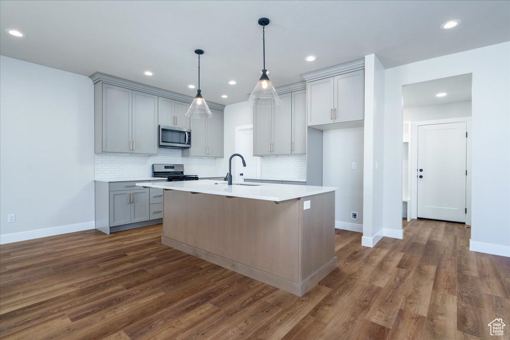 Kitchen with dark hardwood / wood-style flooring, stainless steel appliances, decorative light fixtures, and an island with sink