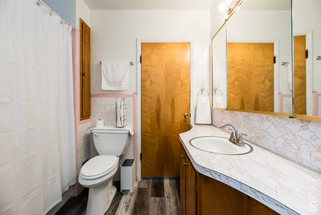 Bathroom with vanity with extensive cabinet space, hardwood / wood-style floors, tile walls, toilet, and backsplash