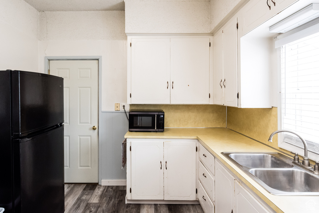 Kitchen with sink, dark hardwood / wood-style floors, white cabinets, and black fridge