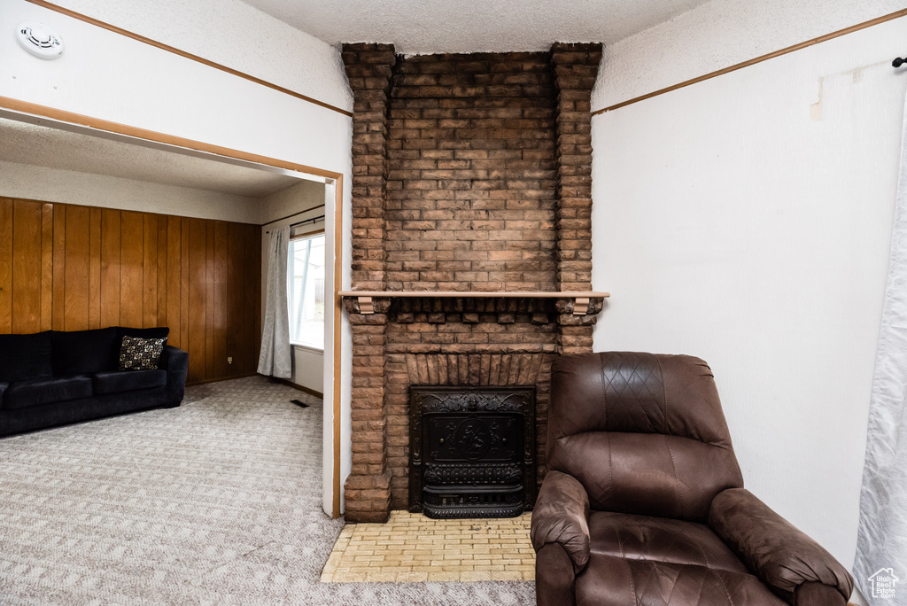 Living room with brick wall, a fireplace, a textured ceiling, wooden walls, and light colored carpet
