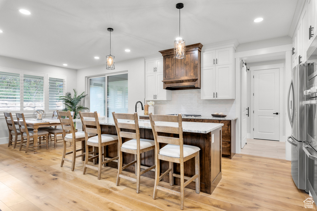 Kitchen with white cabinets, light stone countertops, decorative light fixtures, and light hardwood / wood-style floors