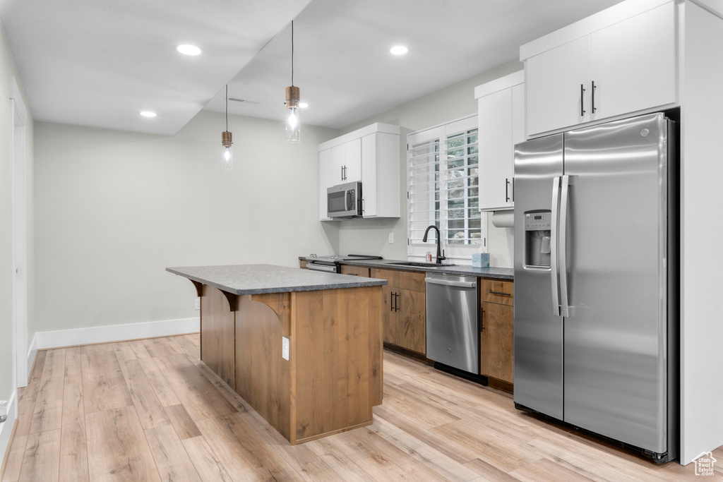Kitchen with appliances with stainless steel finishes, decorative light fixtures, a center island, light hardwood / wood-style floors, and white cabinetry