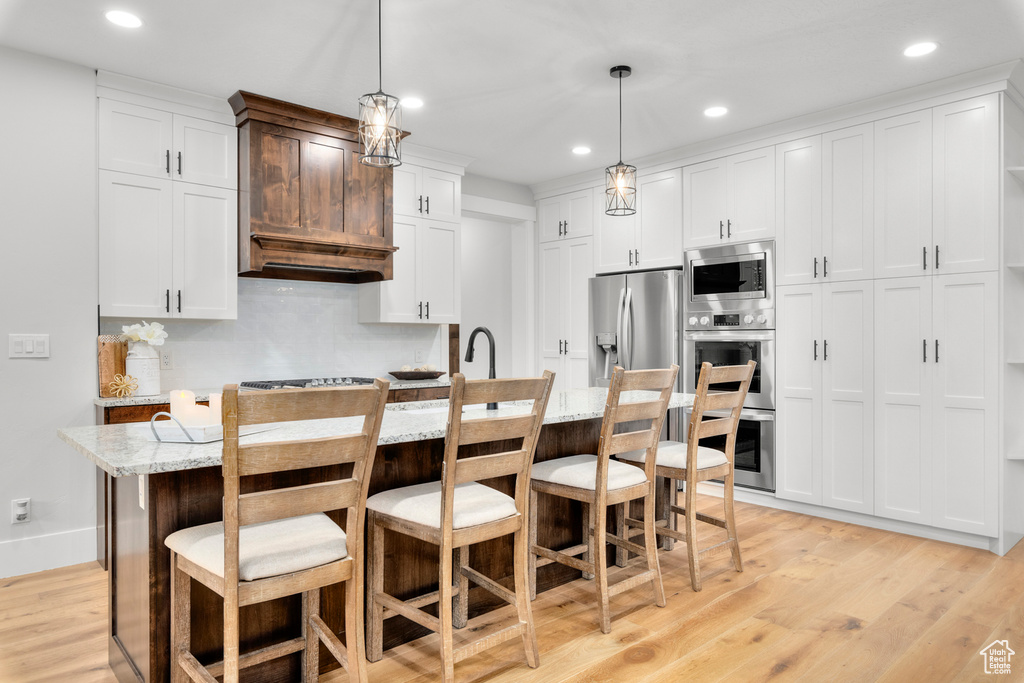 Kitchen featuring decorative light fixtures, appliances with stainless steel finishes, a center island with sink, light hardwood / wood-style floors, and a breakfast bar area