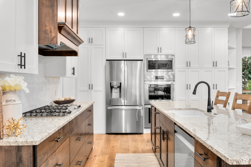 Kitchen featuring custom range hood, white cabinets, stainless steel appliances, sink, and light hardwood / wood-style flooring