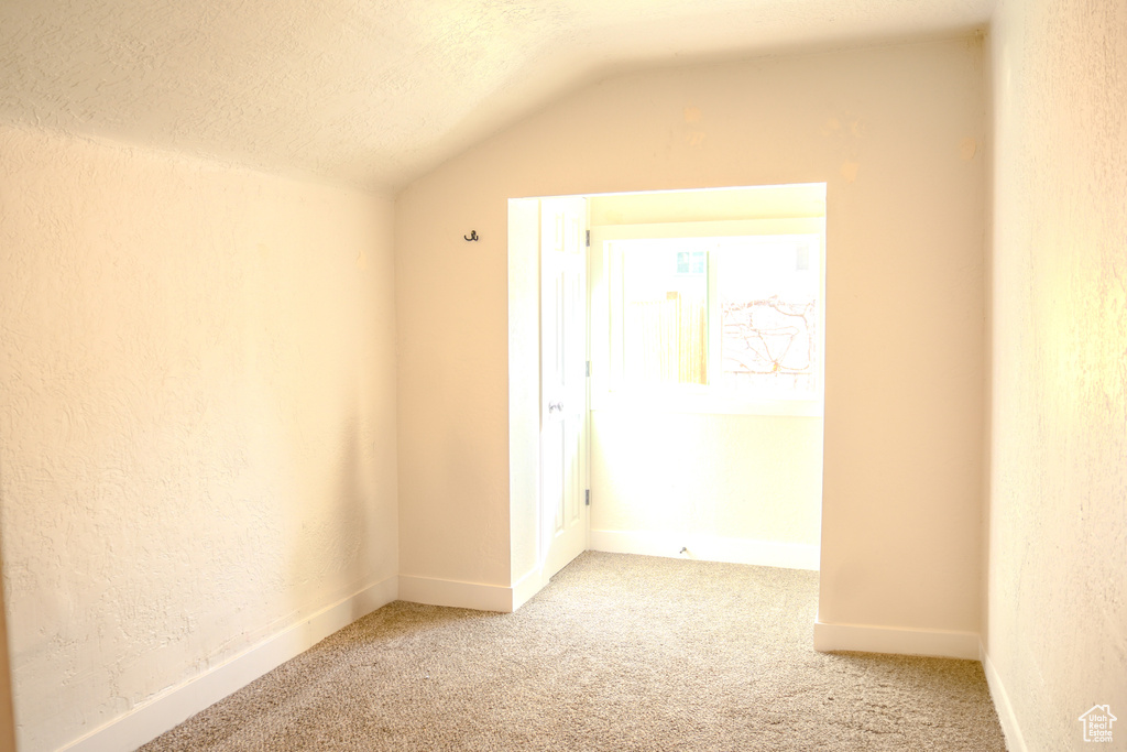 Carpeted spare room featuring vaulted ceiling and a textured ceiling