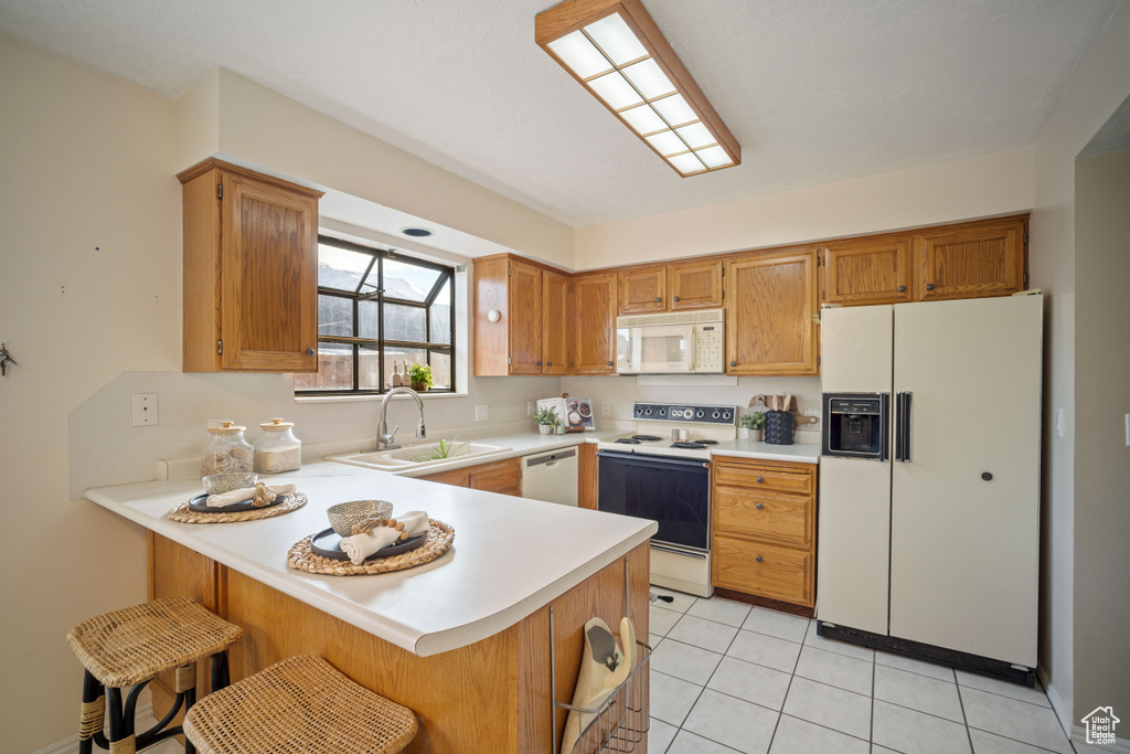 Kitchen featuring kitchen peninsula, light tile flooring, white appliances, a breakfast bar, and sink
