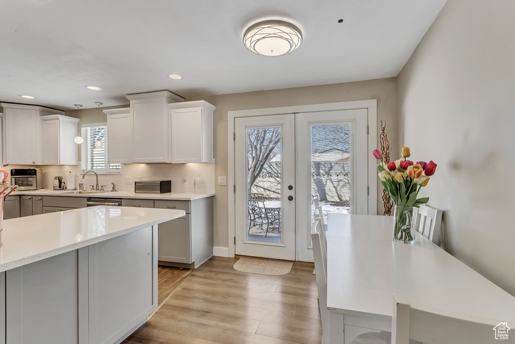 Kitchen with sink, white cabinets, light hardwood / wood-style floors, backsplash, and stainless steel dishwasher