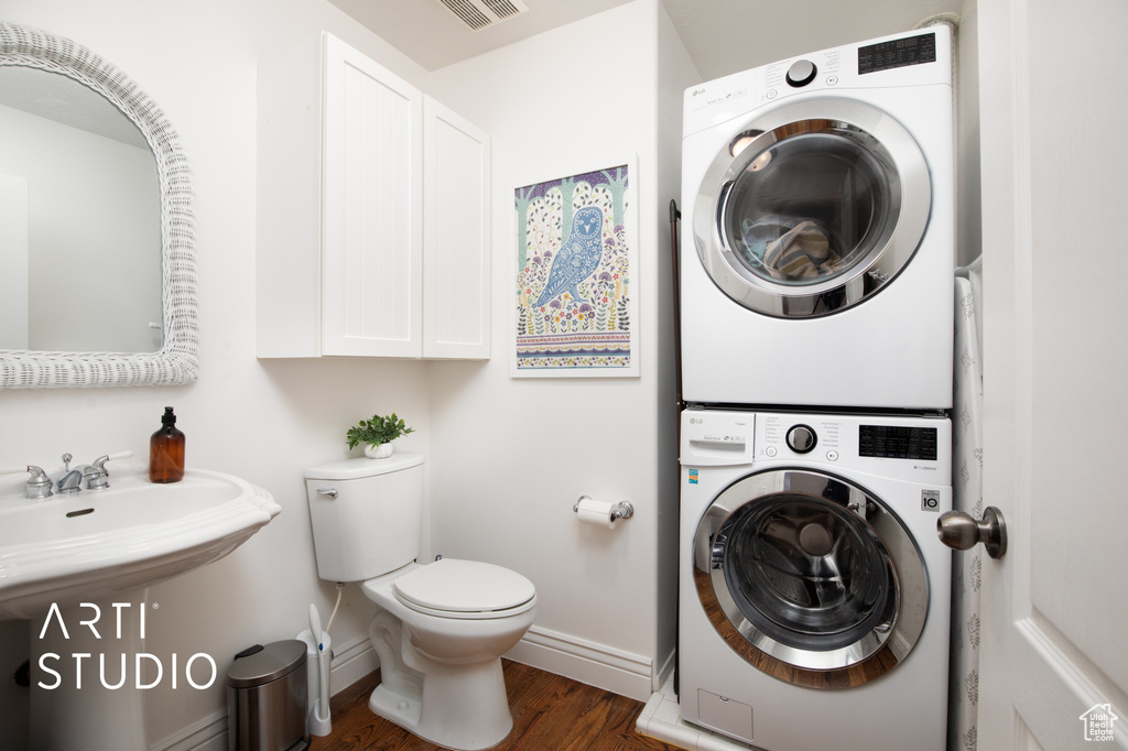 Laundry area with dark hardwood / wood-style flooring and stacked washing maching and dryer