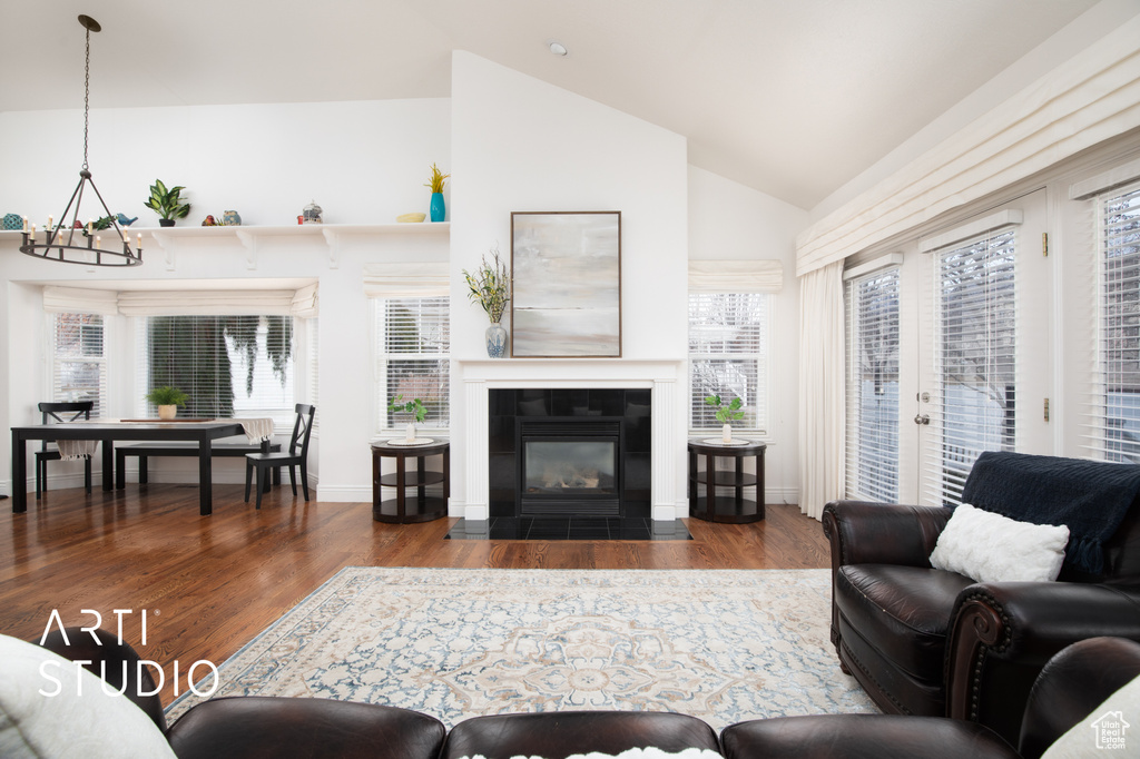 Living room featuring vaulted ceiling, a tiled fireplace, dark hardwood / wood-style floors, and an inviting chandelier