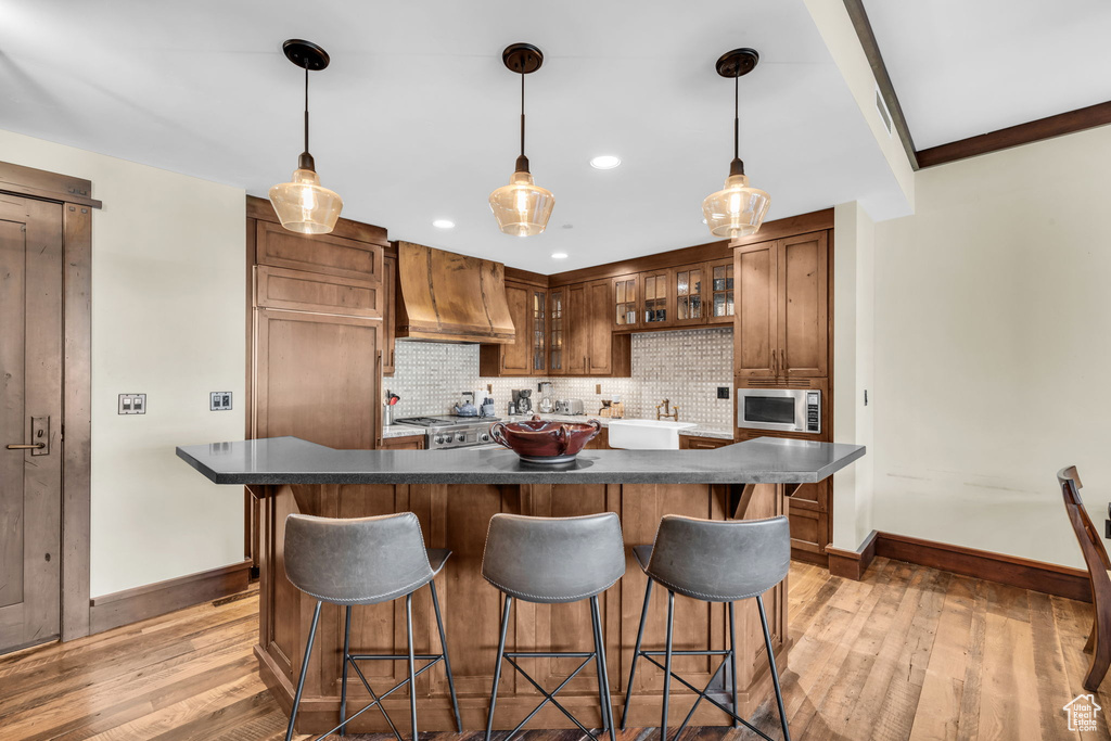 Kitchen featuring backsplash, premium range hood, stainless steel microwave, light hardwood / wood-style floors, and a kitchen island