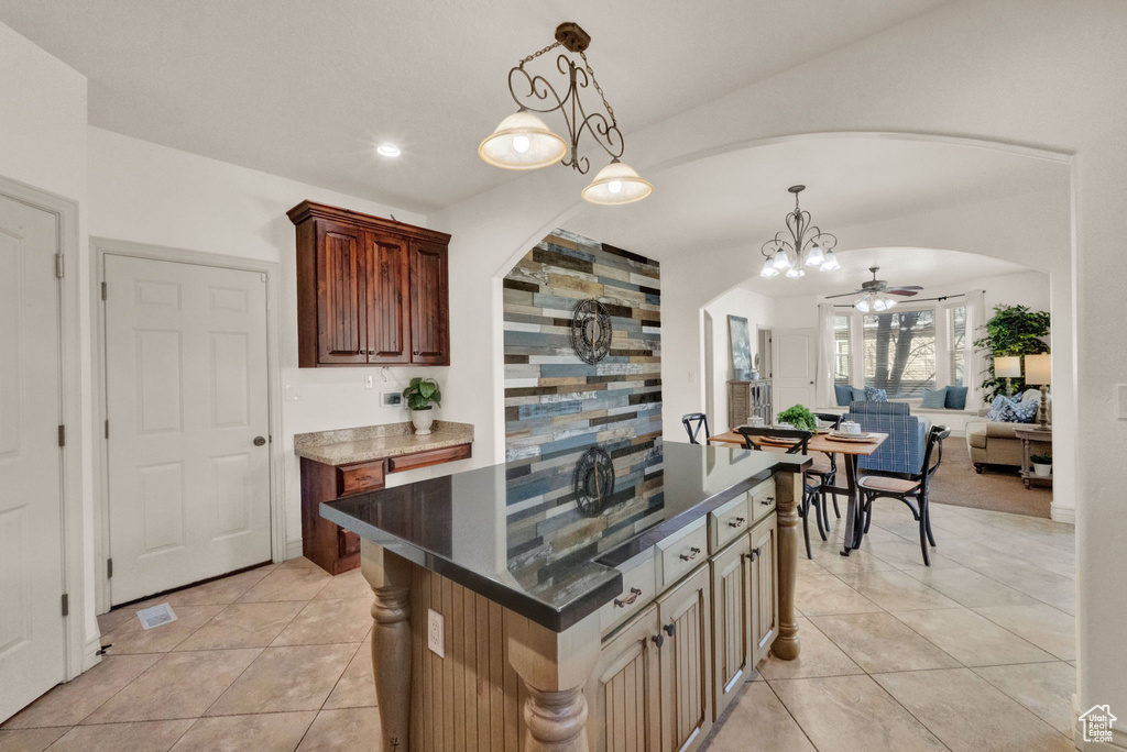 Kitchen with light tile floors, ceiling fan with notable chandelier, hanging light fixtures, and a center island
