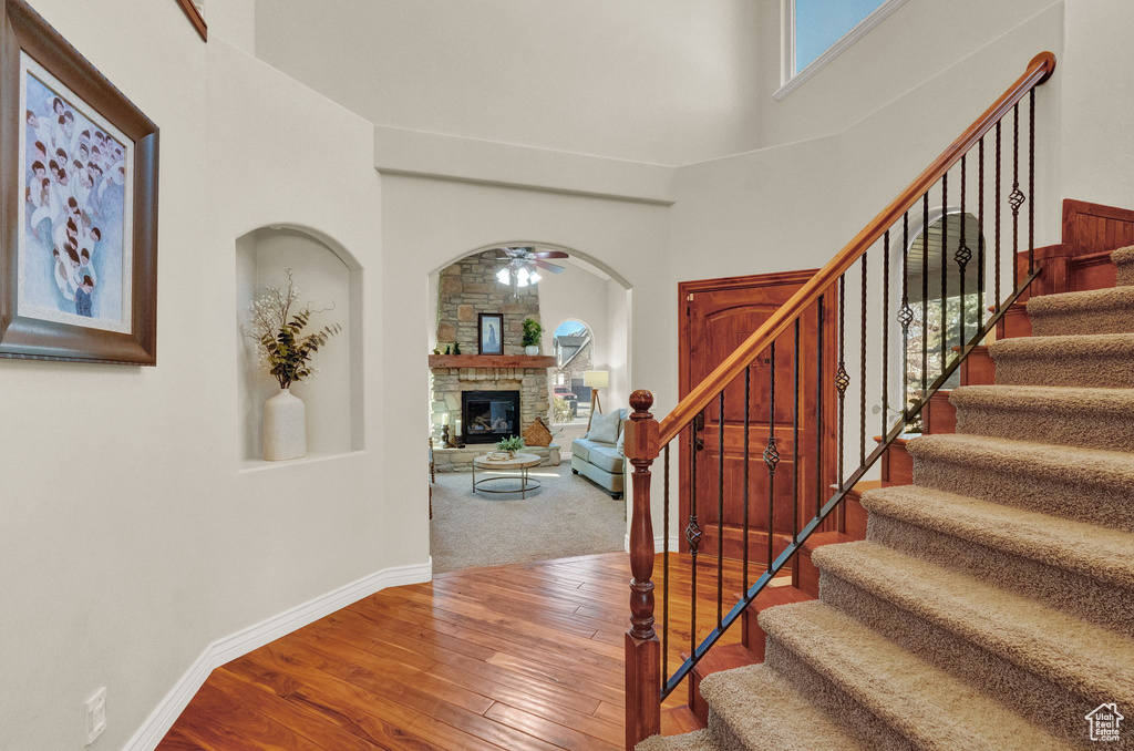 Staircase with a high ceiling, a stone fireplace, carpet flooring, and ceiling fan