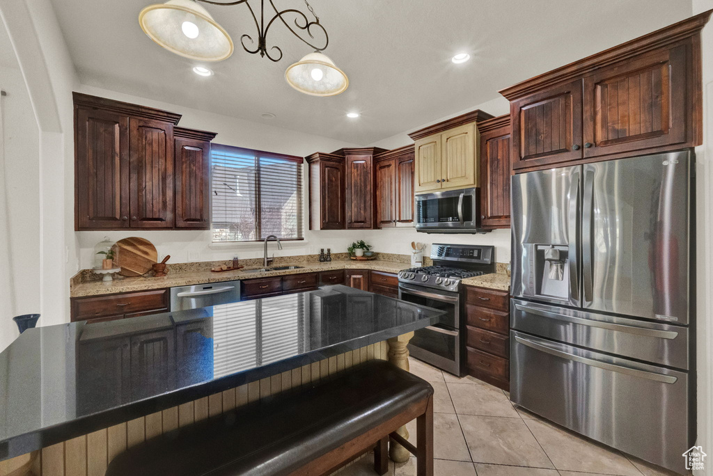 Kitchen featuring sink, dark stone counters, light tile floors, stainless steel appliances, and a breakfast bar area