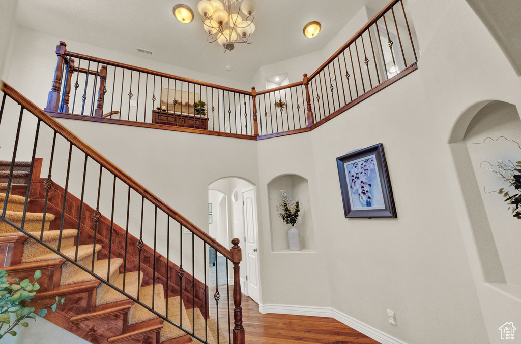 Stairs featuring a notable chandelier, dark hardwood / wood-style floors, and a high ceiling