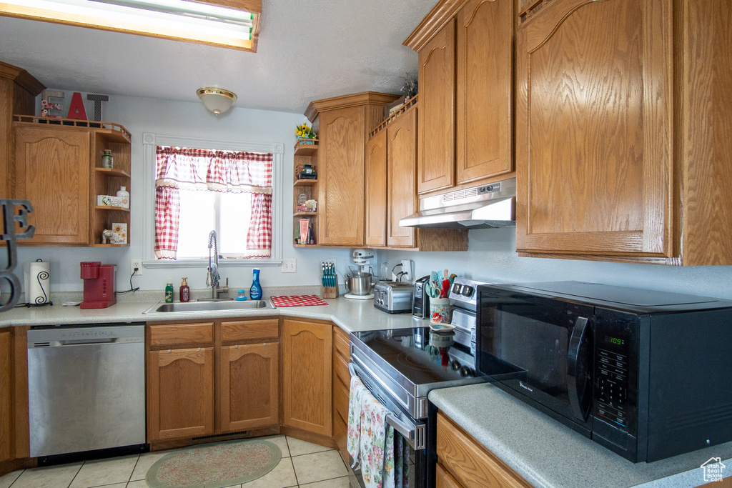 Kitchen featuring sink, dishwasher, light tile floors, and electric range
